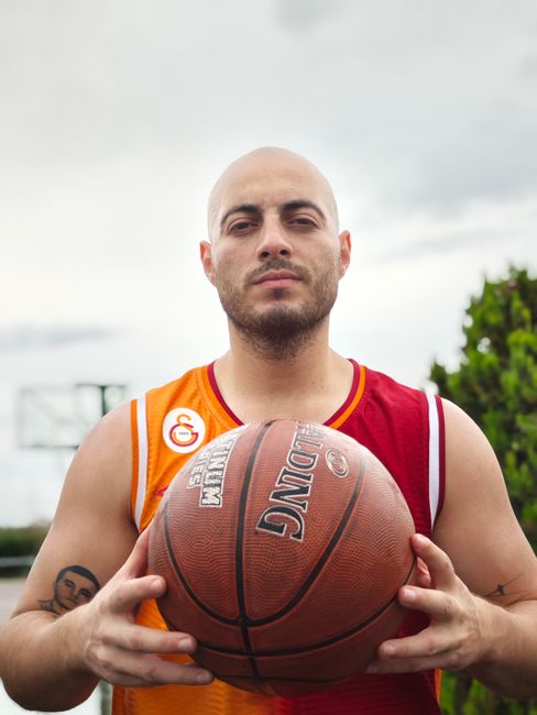 Bald basketball player holding a ball outdoors, showing determination.