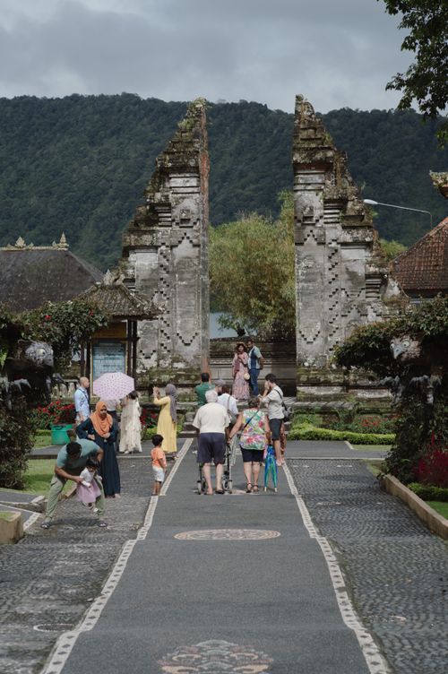 Free A group of tourists explore an ancient temple gateway in Bali, Indonesia, surrounded by lush greenery. Stock Photo
