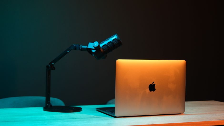 Illuminated modern podcast setup with a microphone and laptop on a wooden desk.