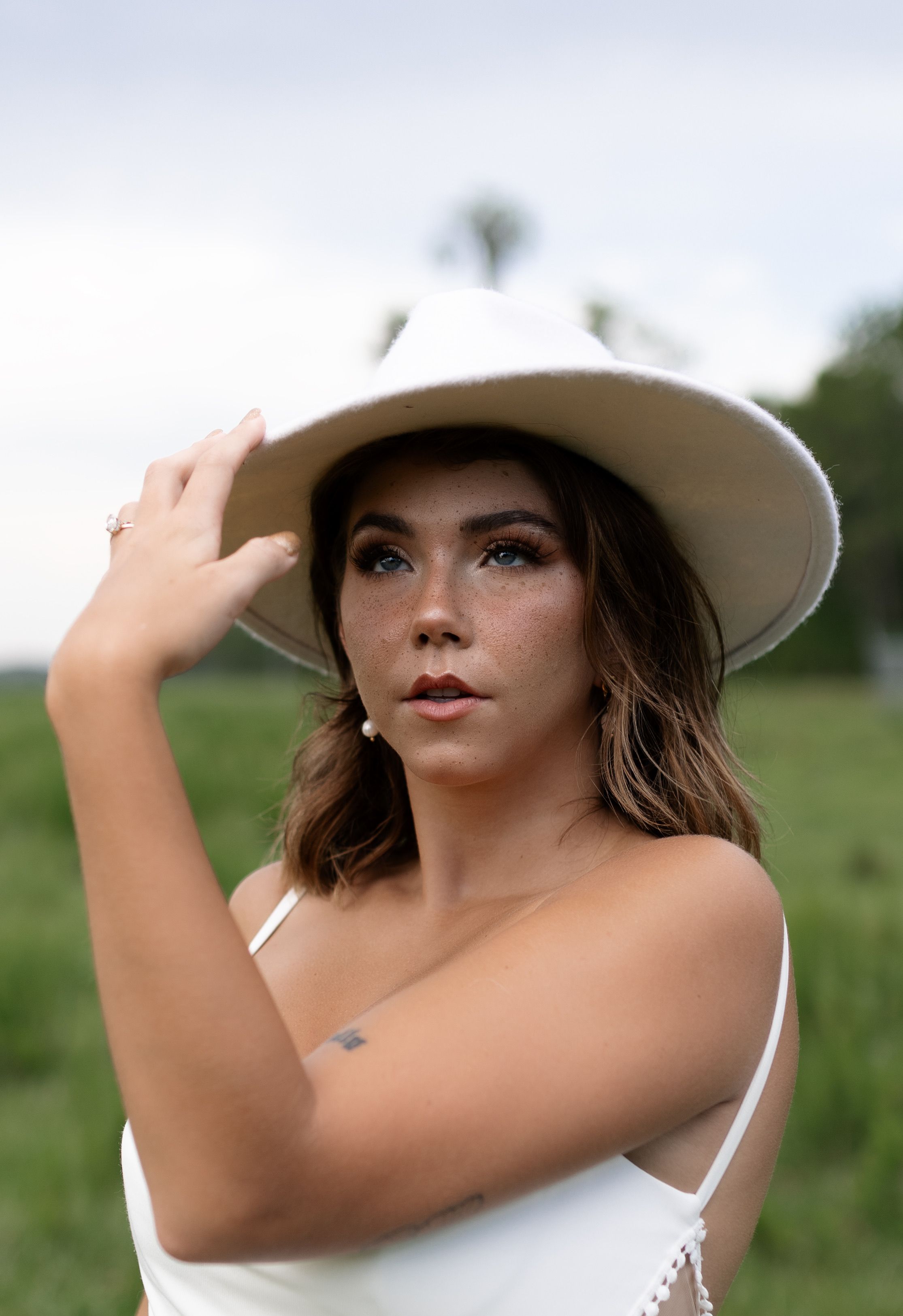Portrait of a young woman outdoors wearing a white hat and dress with a serene expression.