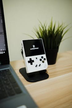 A sleek handheld console displayed on a desk next to a laptop and plant, emphasizing modern gaming technology.