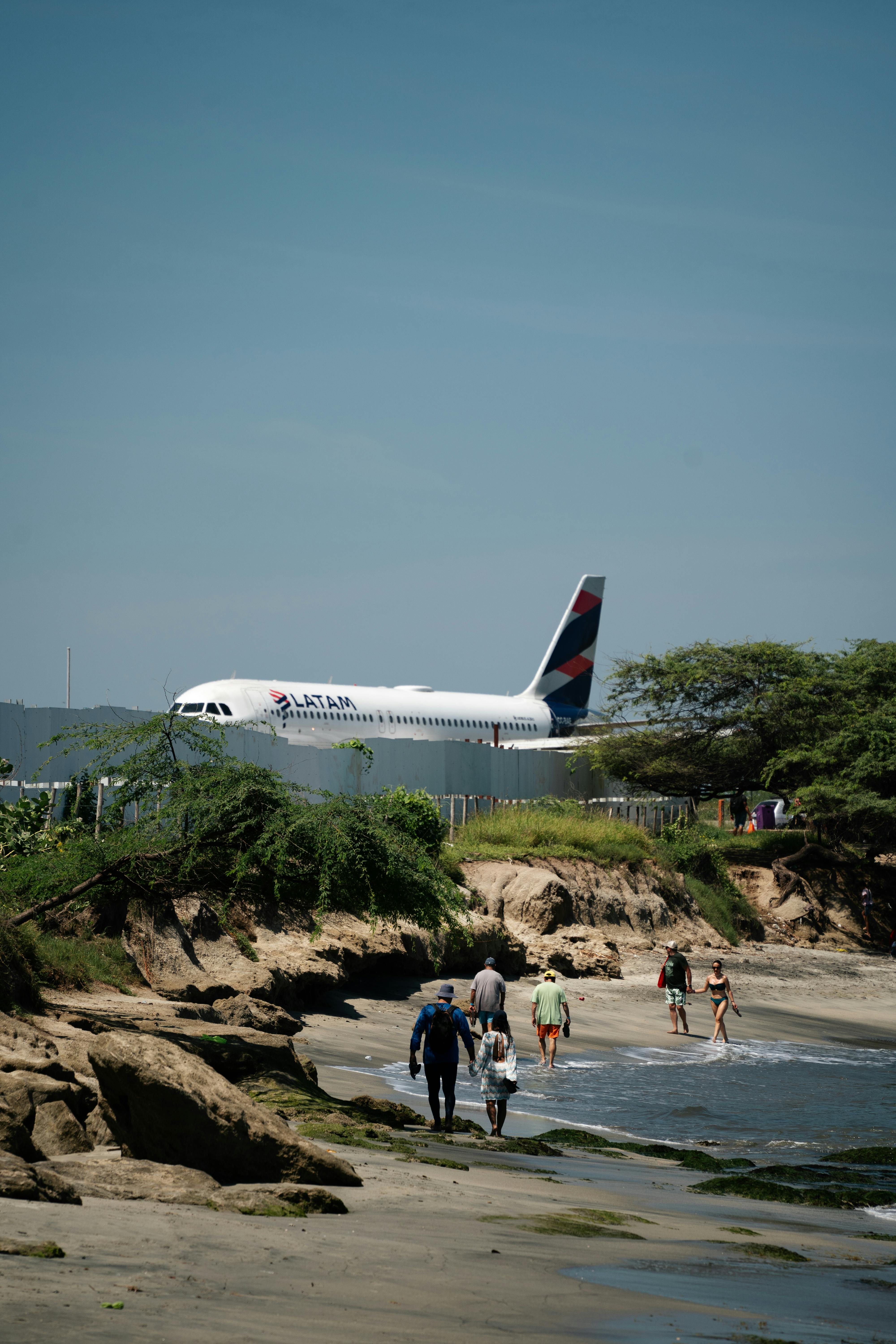 Commercial airplane landing near Santa Marta beach with beachgoers visible.