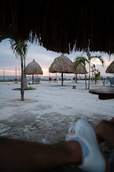Peaceful beachfront setting with thatched umbrellas and subtle sunset over the horizon.