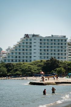 Hotel by the beach with people enjoying a sunny day by the sea.