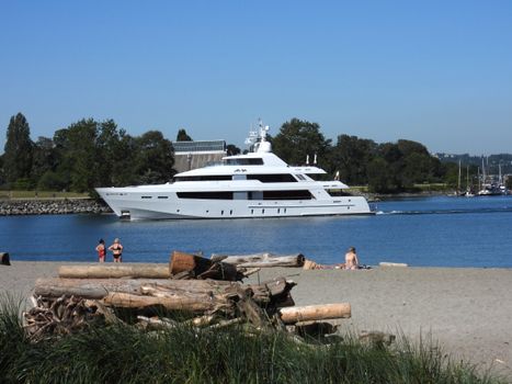 Luxurious white yacht sailing near Vancouver's sandy beach on a sunny summer day.