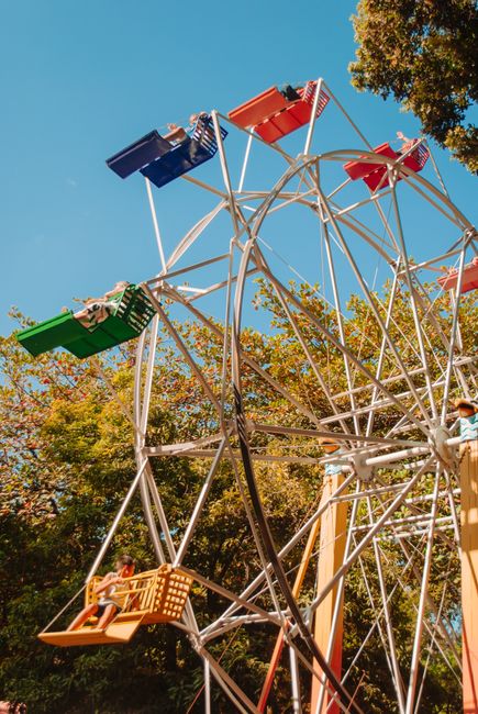 Colorful ferris wheel in an outdoor fairground under a bright blue sky, capturing a fun leisure moment.