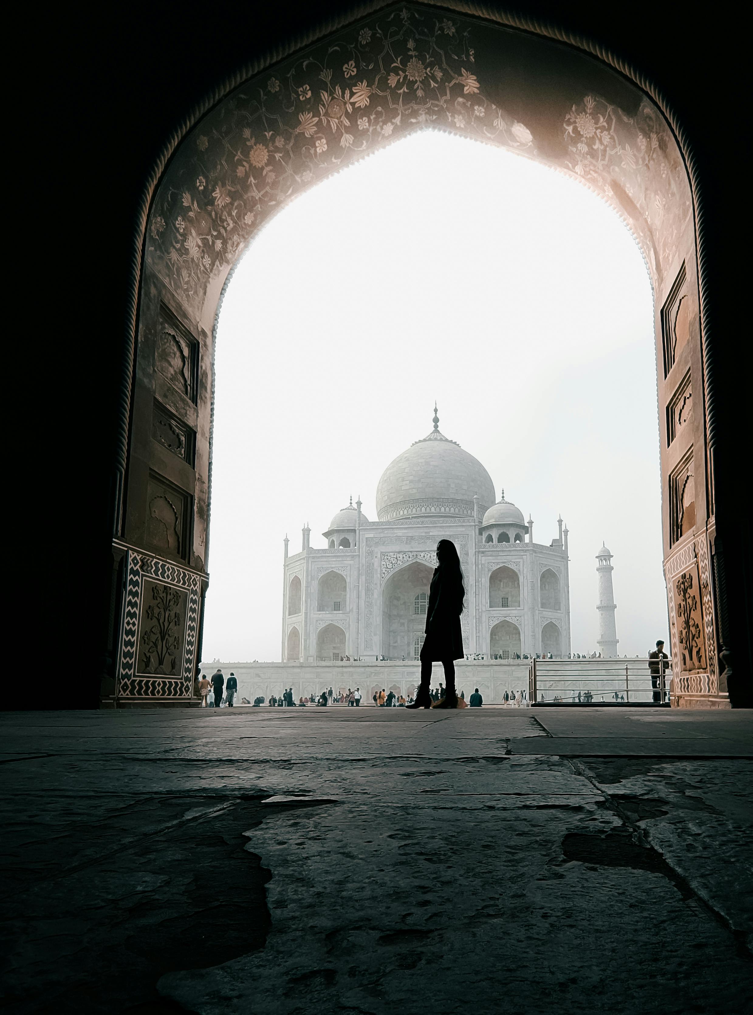A traveler silhouetted at the grand entrance of the Taj Mahal, Agra, India, showcasing exquisite Mughal architecture.