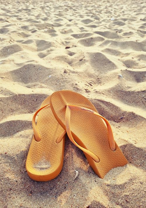 Free A pair of yellow flip flops on a sandy beach, capturing a sunny summer vibe. Stock Photo