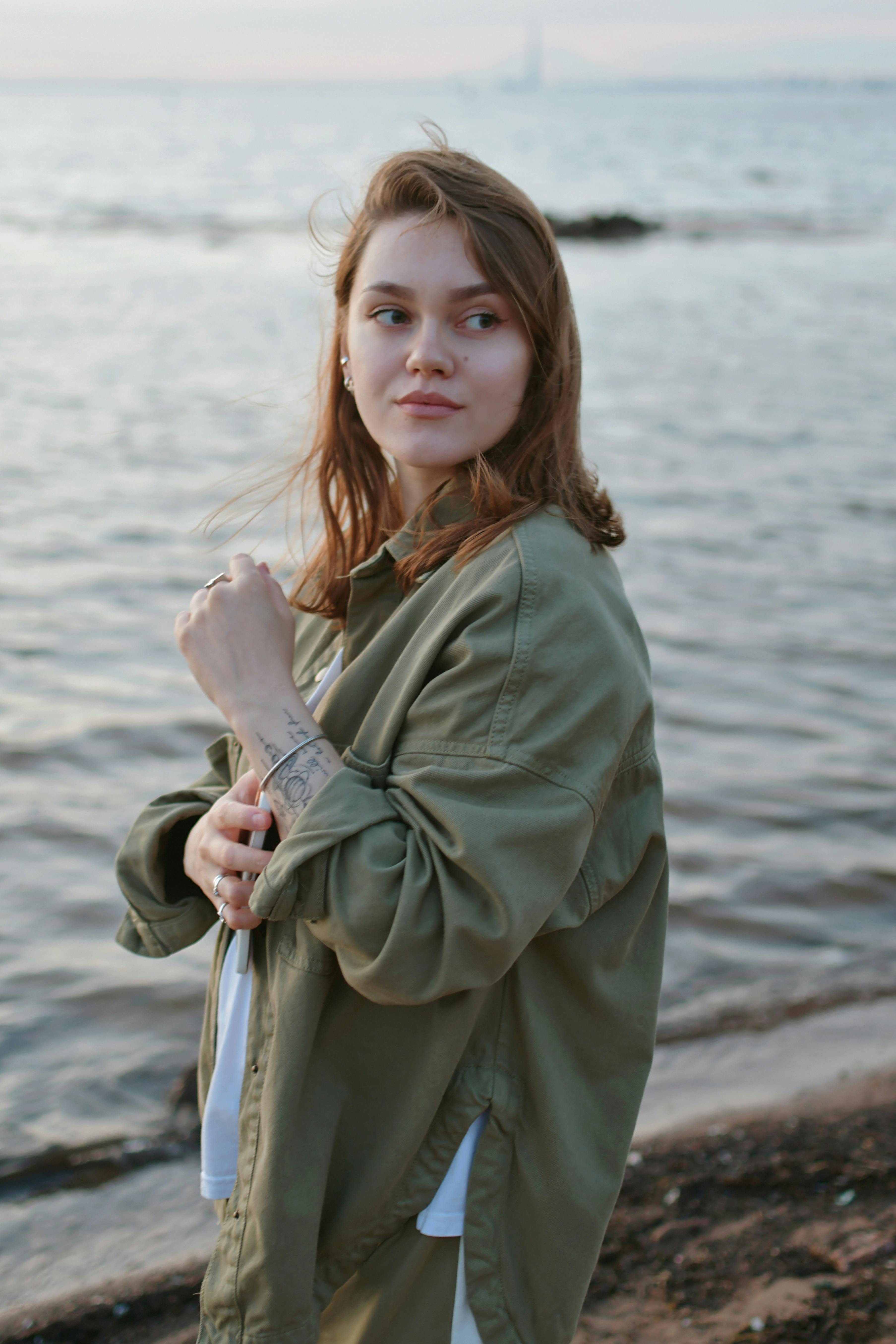 a woman in an olive green jacket standing by the water