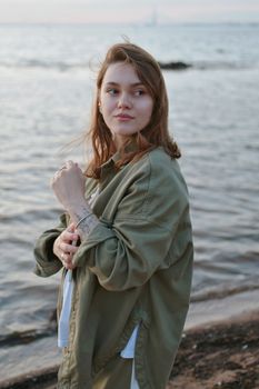 Woman in casual jacket enjoys a peaceful moment by the sea at sunset.
