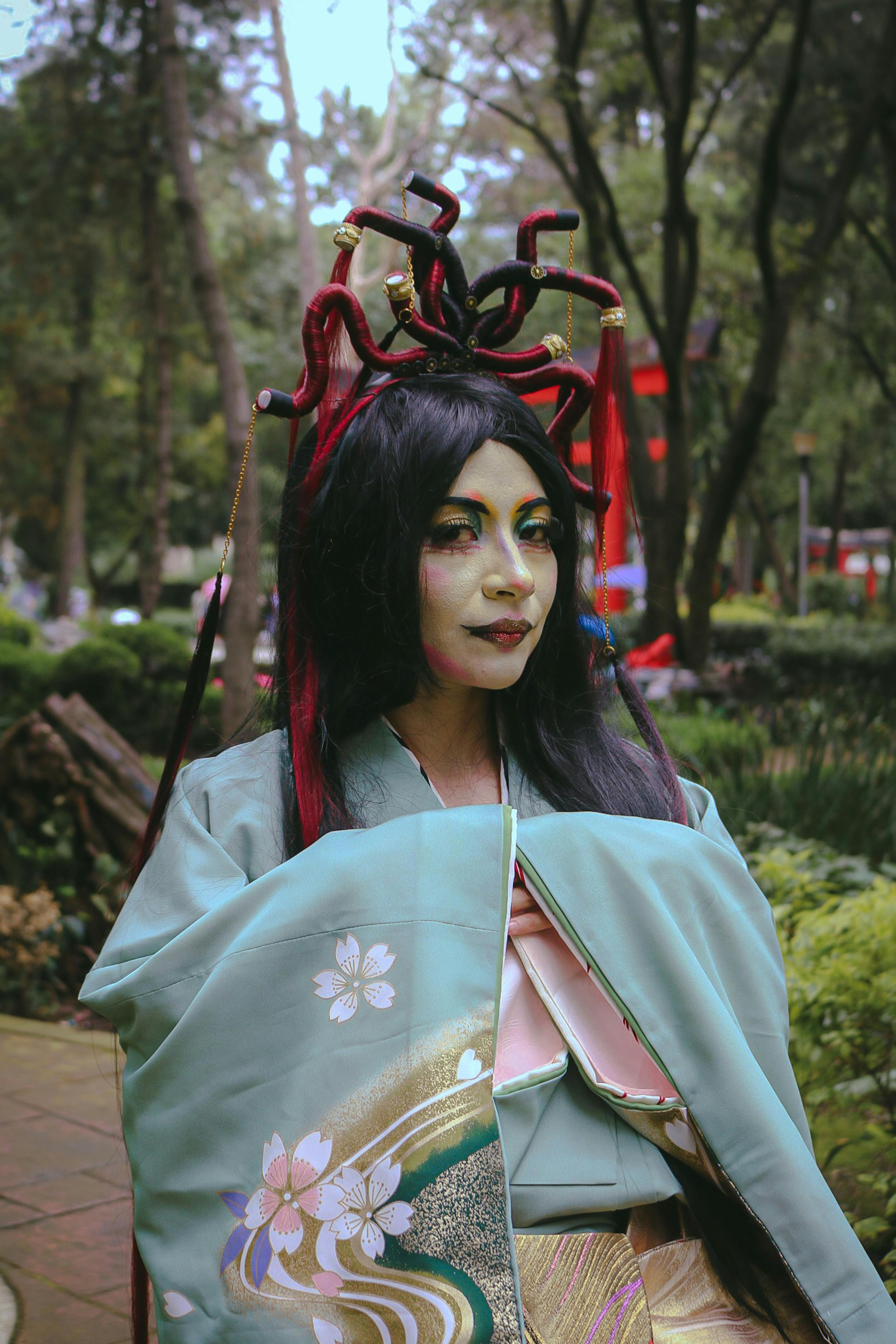 Portrait of a woman in traditional costume outdoors, showcasing vivid makeup and intricate hair design.