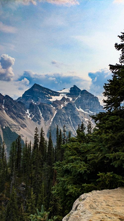 Free Majestic view of snow-covered mountains surrounded by evergreen trees under a cloudy sky. Stock Photo