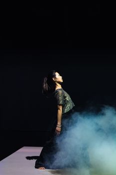 A dancer immersed in a misty stage performance with a dark, dramatic ambiance.
