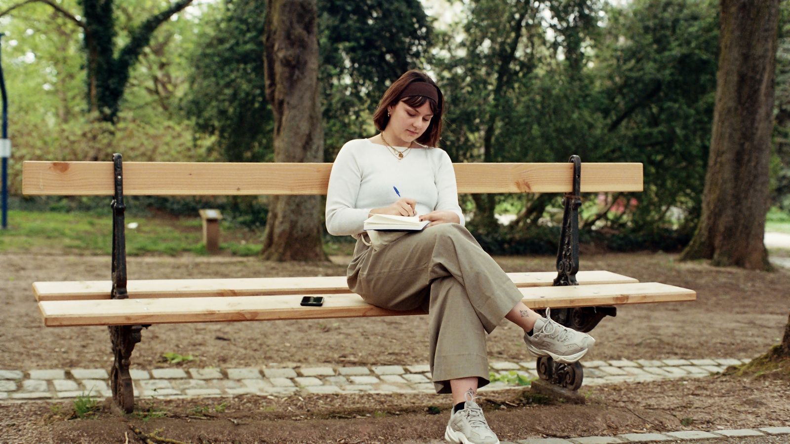 A person writing in a notebook on a park bench