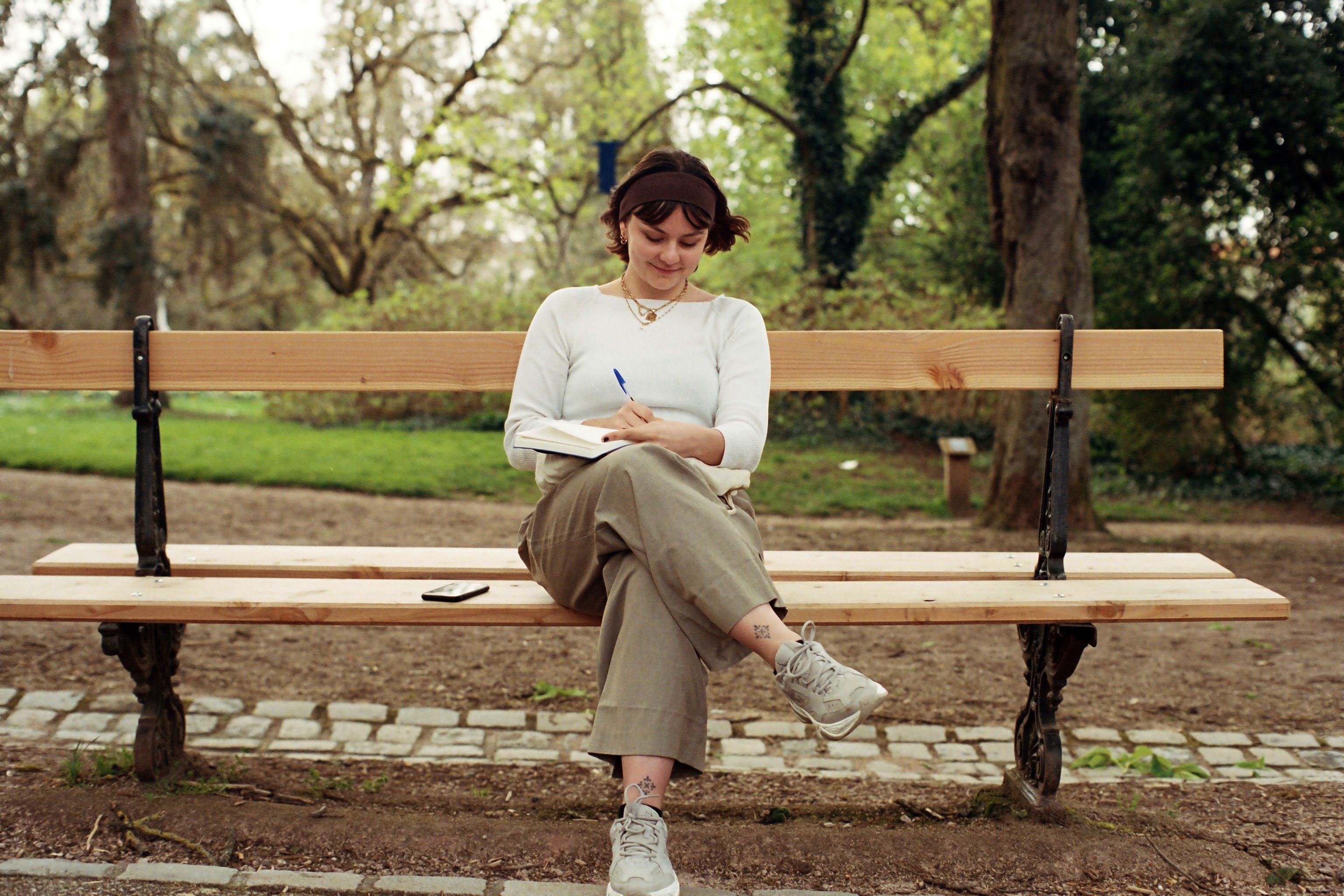 A young woman enjoys writing in a notebook while sitting on a park bench.