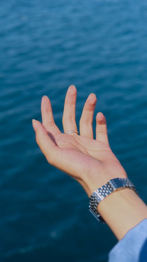 Free A close-up of a hand with a watch reaching towards the blue ocean, symbolizing freedom and exploration. Stock Photo