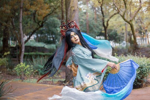 A woman in a traditional blue kimono dances gracefully outdoors, surrounded by nature.