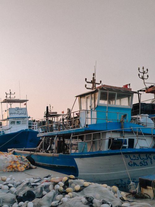 Free Colorful fishing boats docked at sunrise in a quiet coastal harbor, with fishing nets in the foreground. Stock Photo