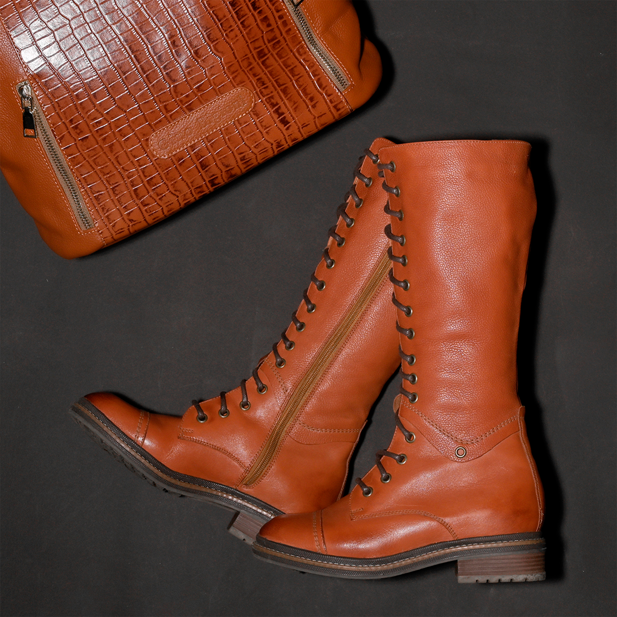 Elegant brown leather boots with lace-up detail beside textured leather handbag.
