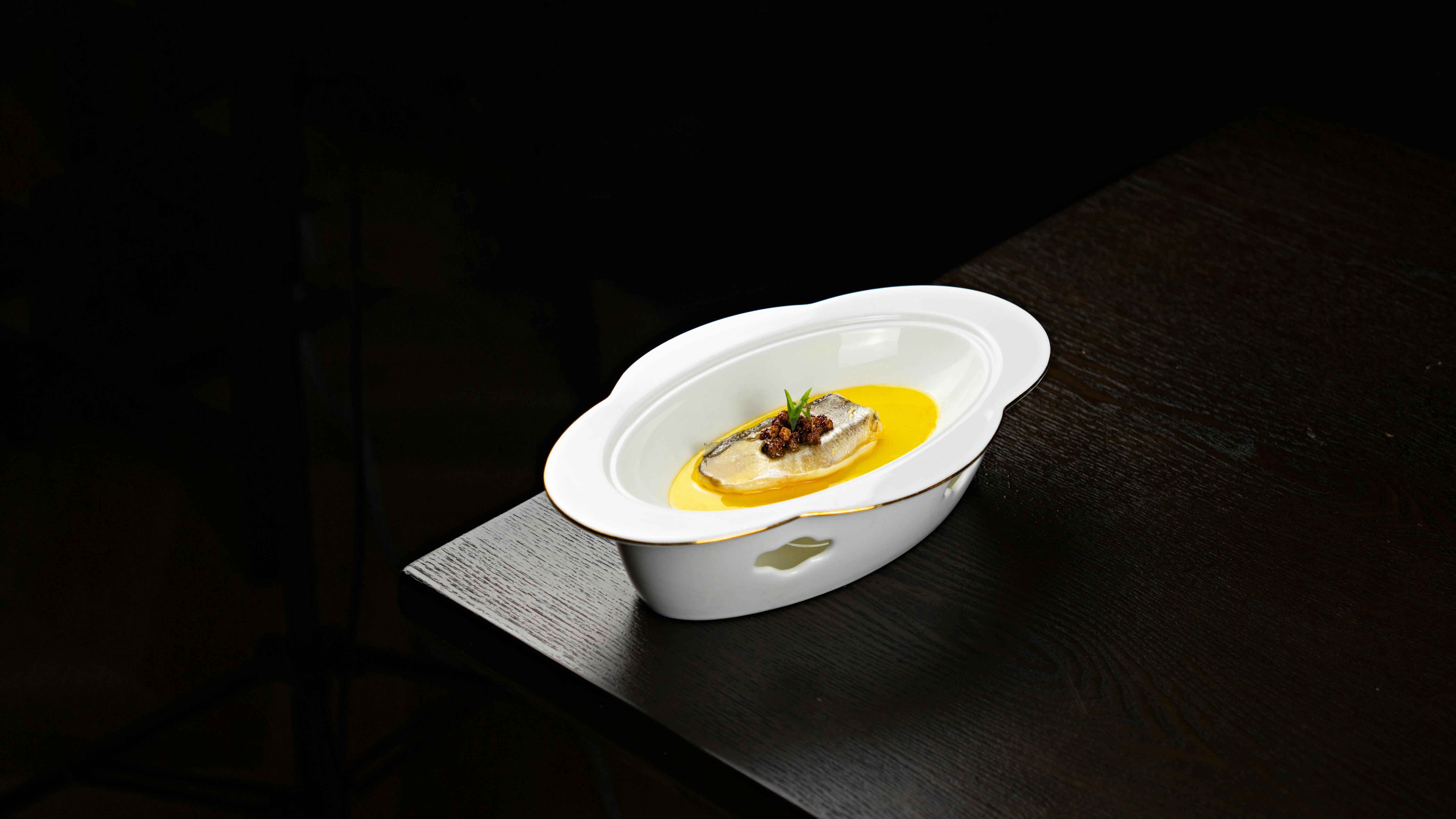 Elegant fish dish with a rich sauce served in a fine white ceramic plate on a dark wooden table.