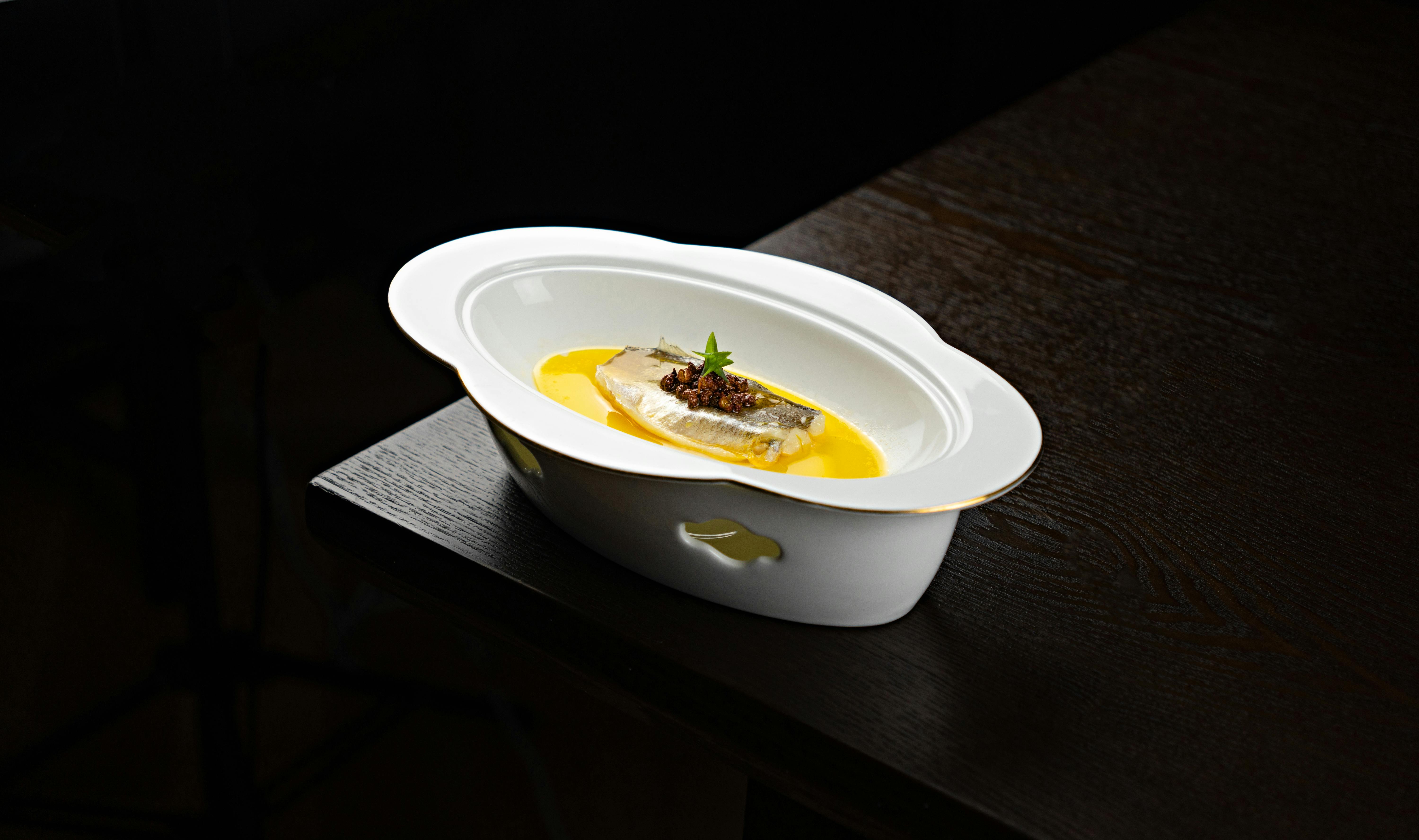 A beautifully plated fish dish with vibrant sauce in an elegant oval white bowl on a dark wooden table.