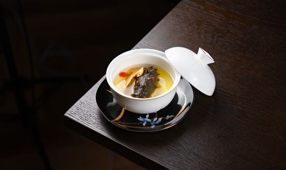 A stylish gourmet soup presented in a porcelain bowl on a dark wooden table.
