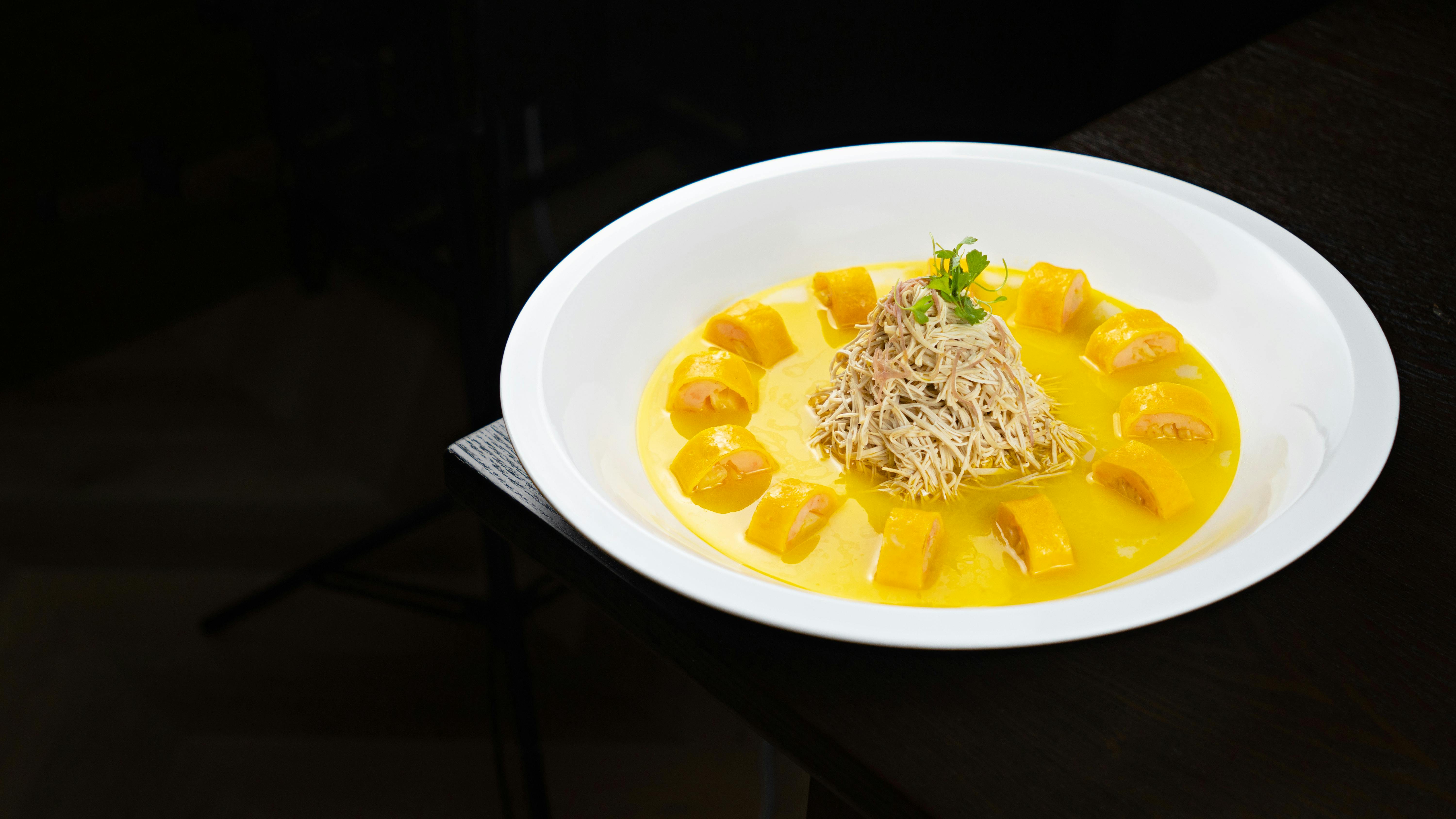 Elegant gourmet dish of chicken with yellow sauce and garnish in a white bowl.