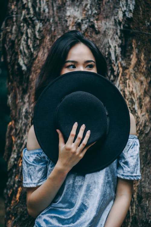 黒い帽子をかぶった木の近くに立っている女性