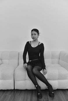 Elegant young woman in fashionable attire posing on a modern sofa in a minimalist setting.