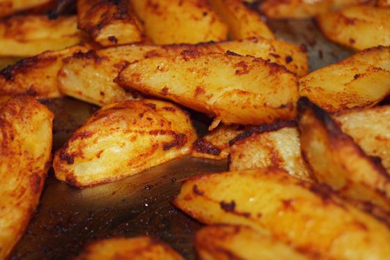 Close view of golden potato wedges with browned paprika-spiced edges on a dark roasting tray