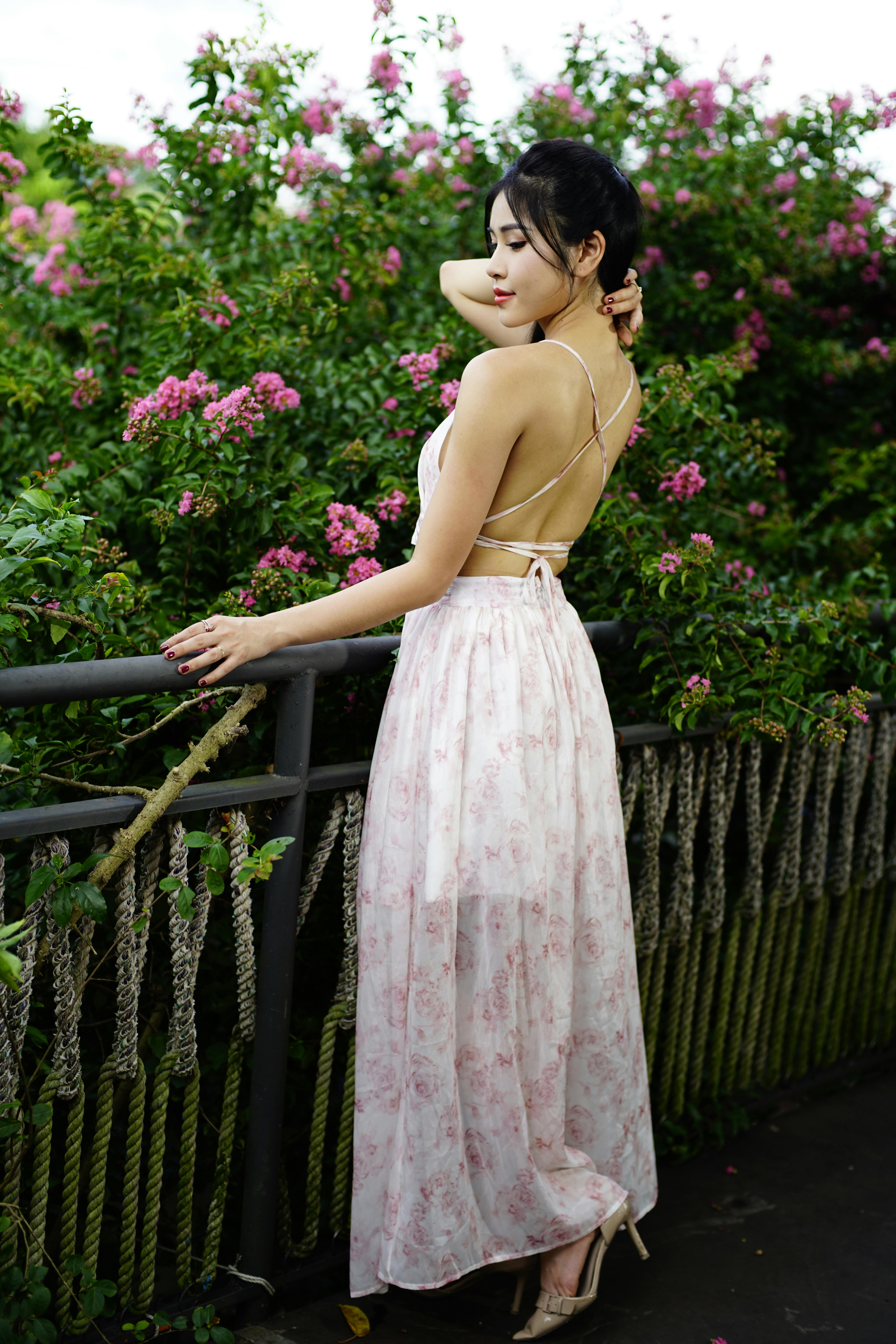A young woman wearing an elegant floral dress posing in a green garden setting.