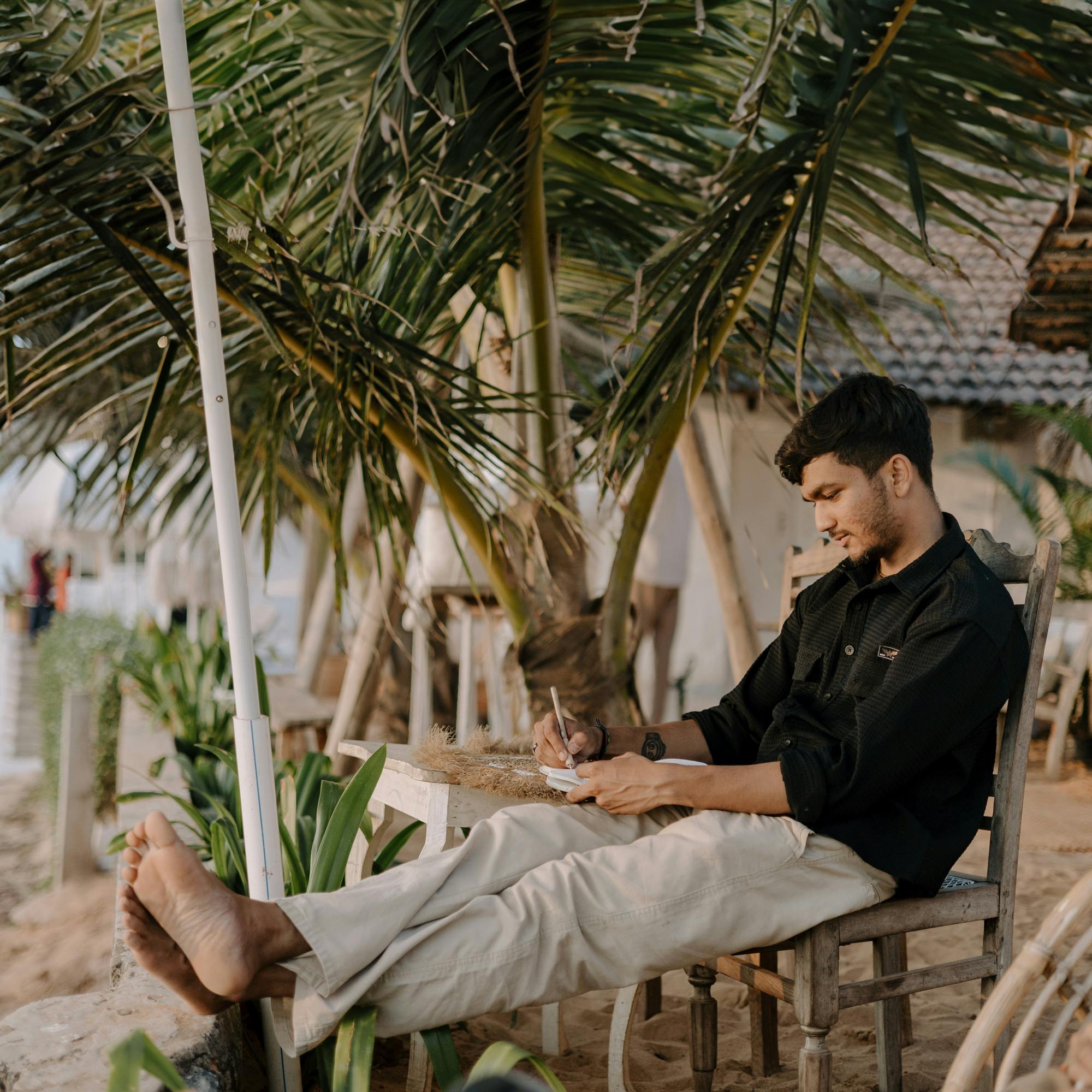 一个年轻人坐在印度果阿海滩的椅子上，正在放松地写作