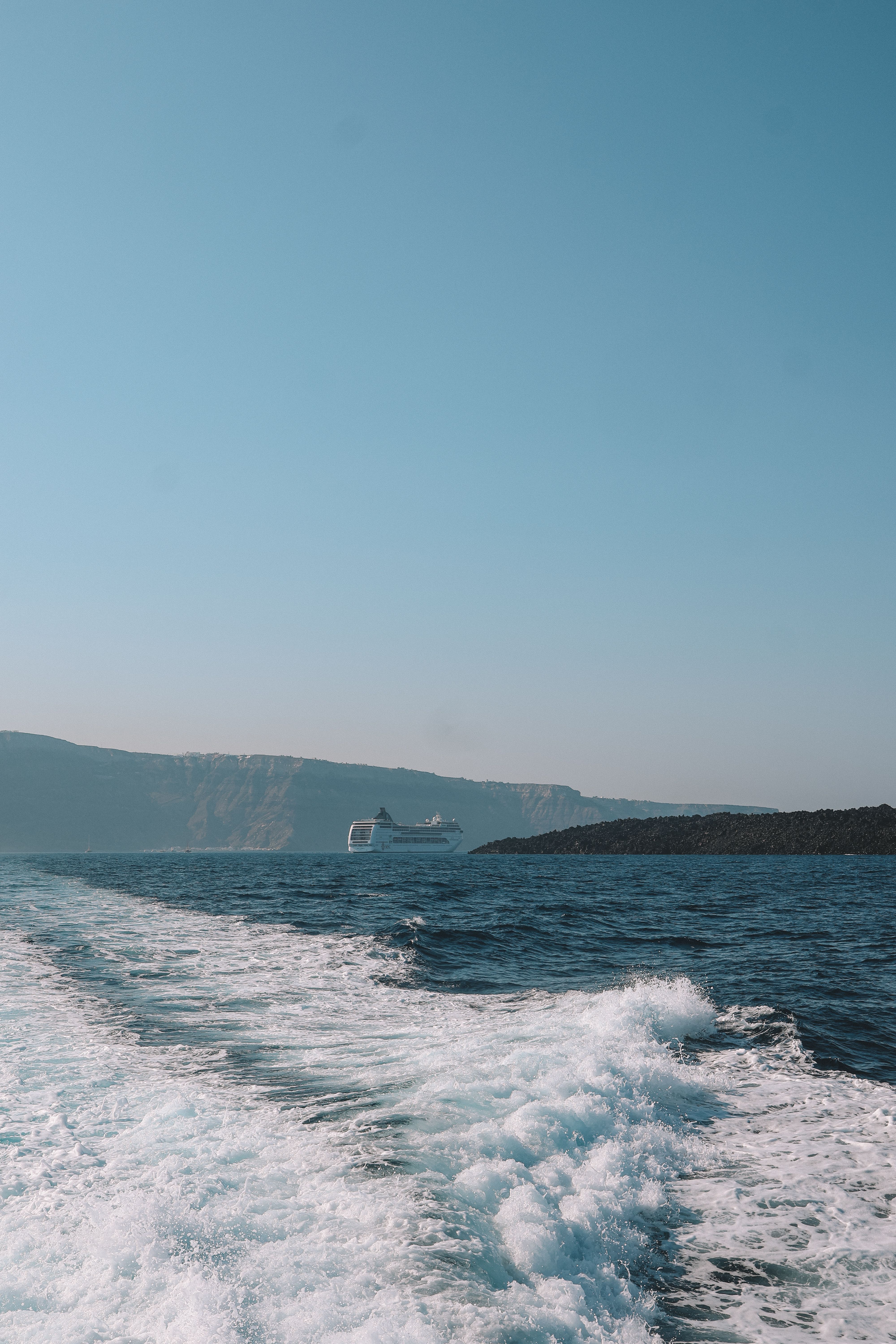 A cruise ship sails near Fira, Greece, leaving a wake in the deep blue ocean.