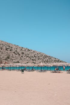 Relaxing beach scene with sun loungers and clear blue waters in Fira, Greece.