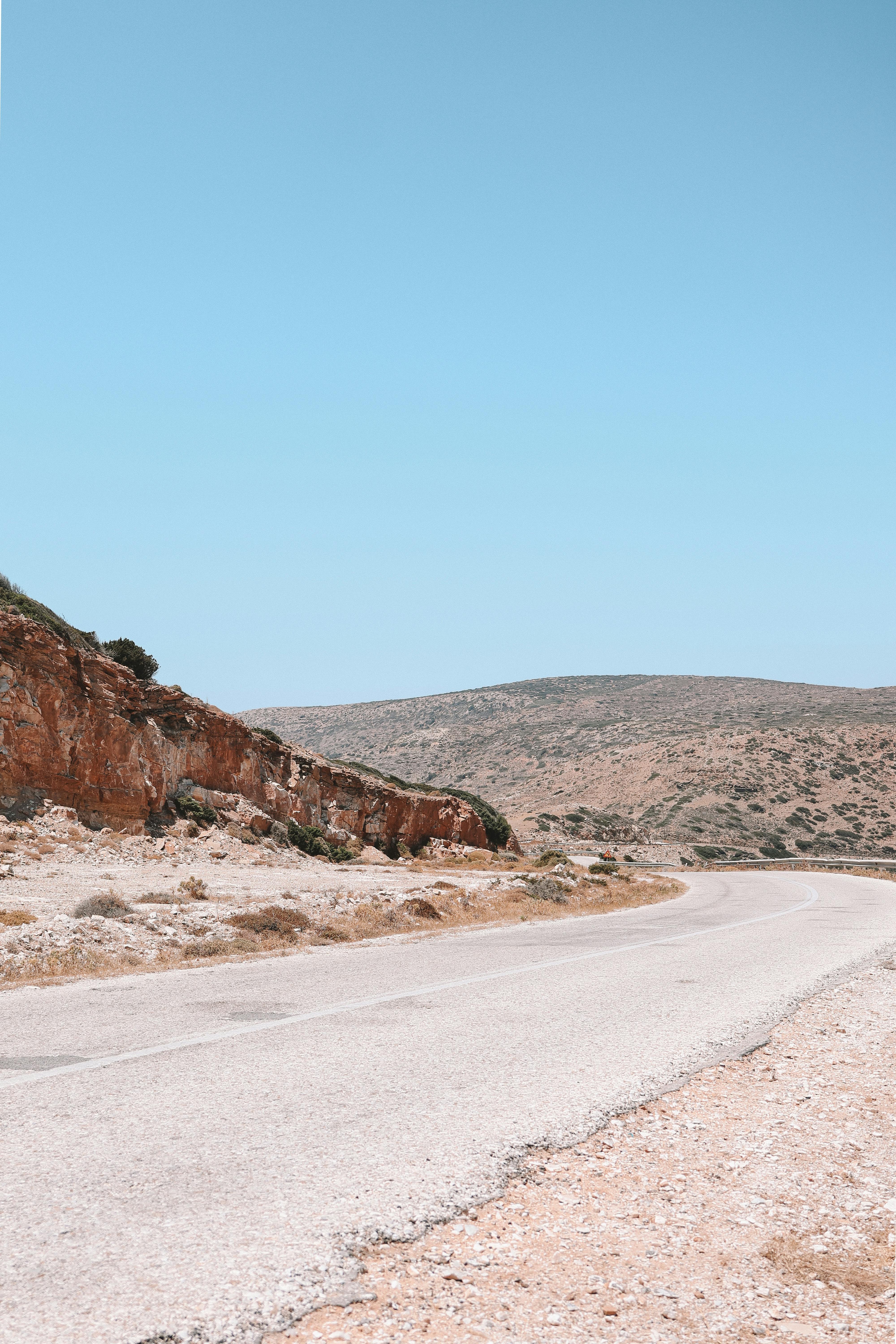 A quiet winding road in Fira, Greece with rocky landscape and clear blue skies.
