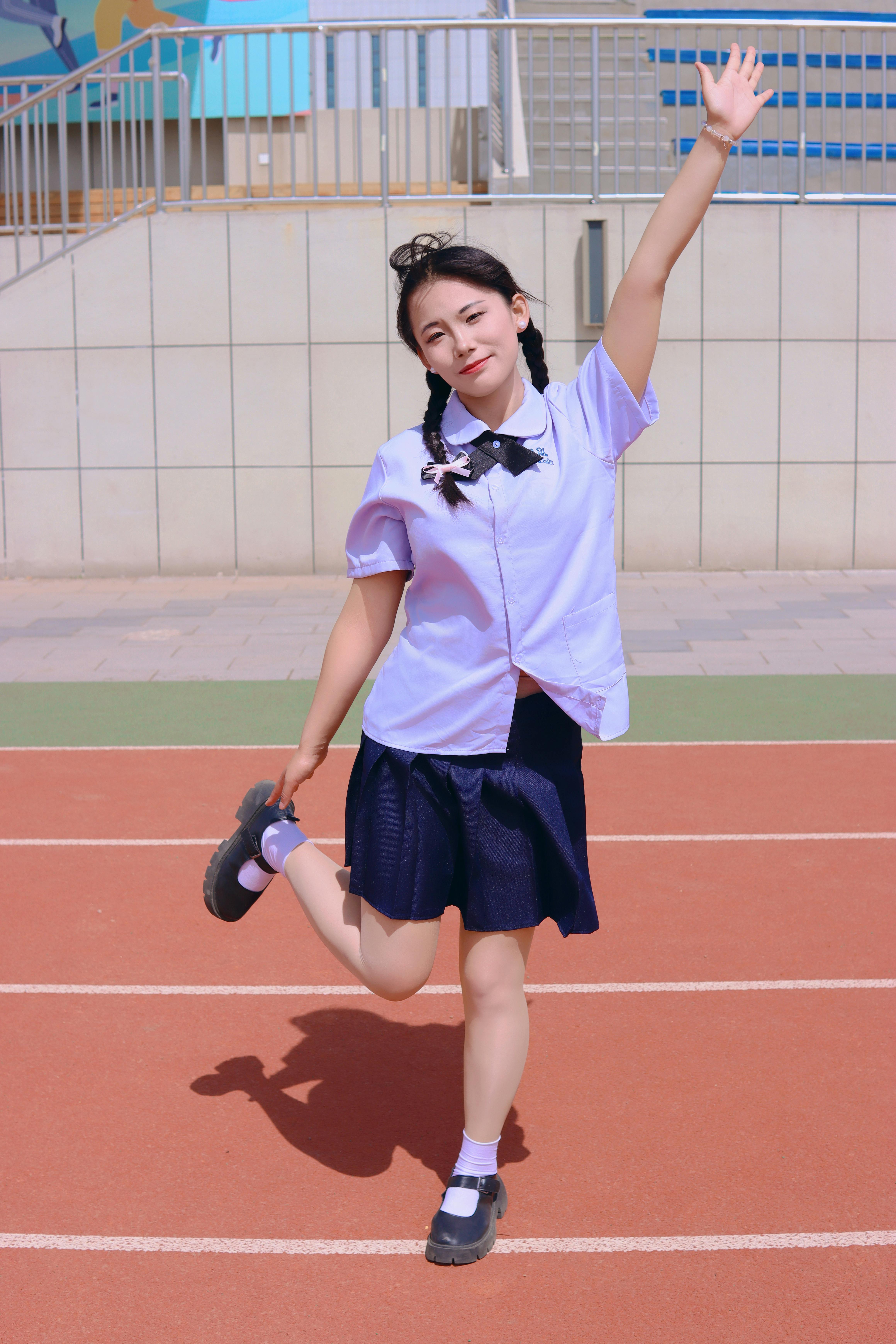 Smiling young woman in a playful pose on an outdoor track, enjoying sunny day.