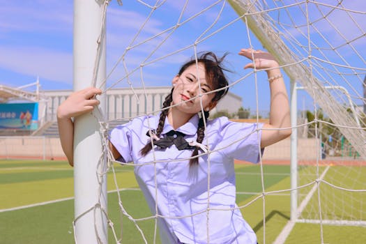 A joyful young woman in a school uniform near a soccer net on a sunny day.