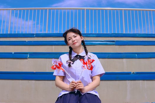 A cheerful young woman holding pinwheels, sitting on outdoor stadium steps.