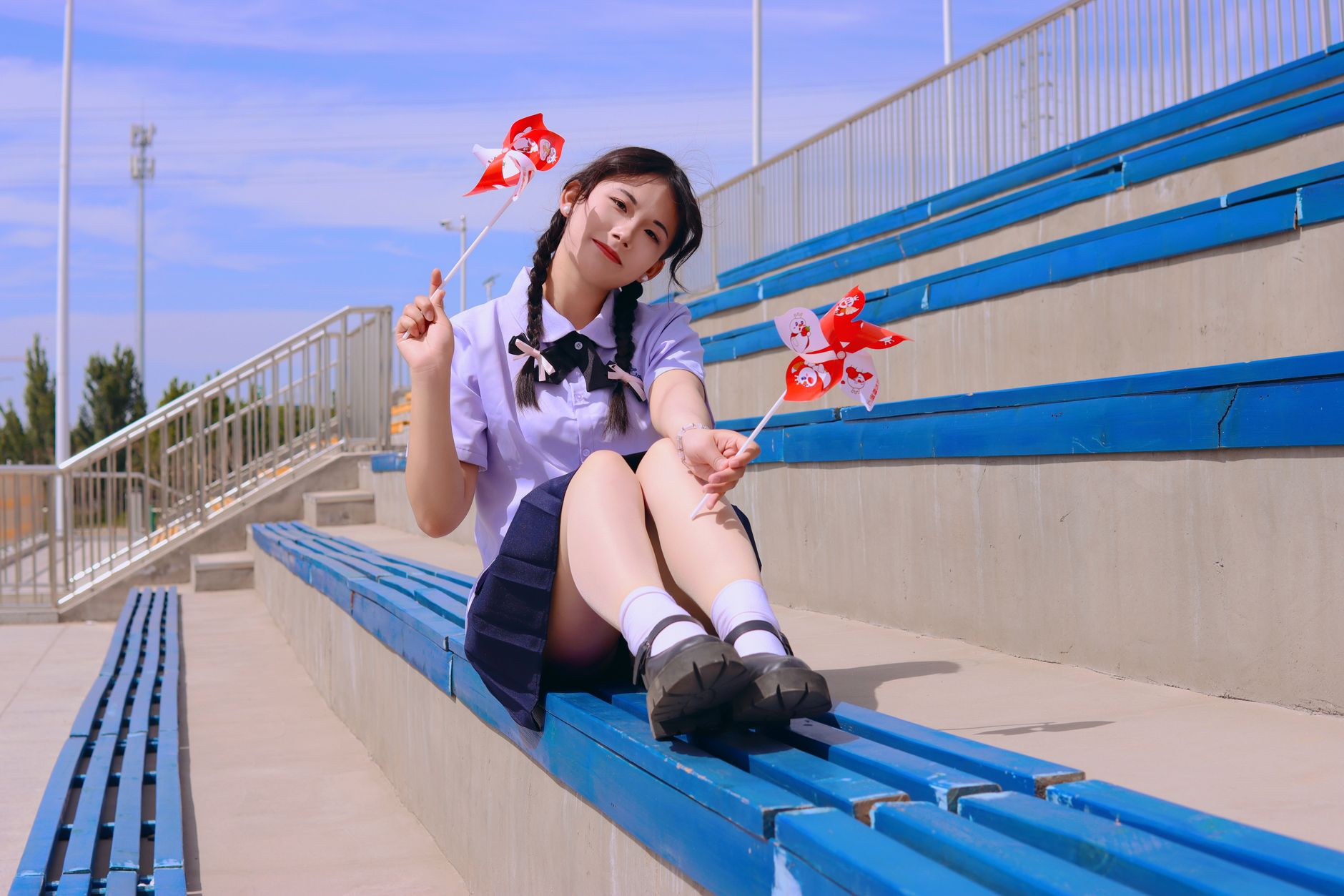 A young woman sitting on bleachers with pinwheels, enjoying a sunny day.