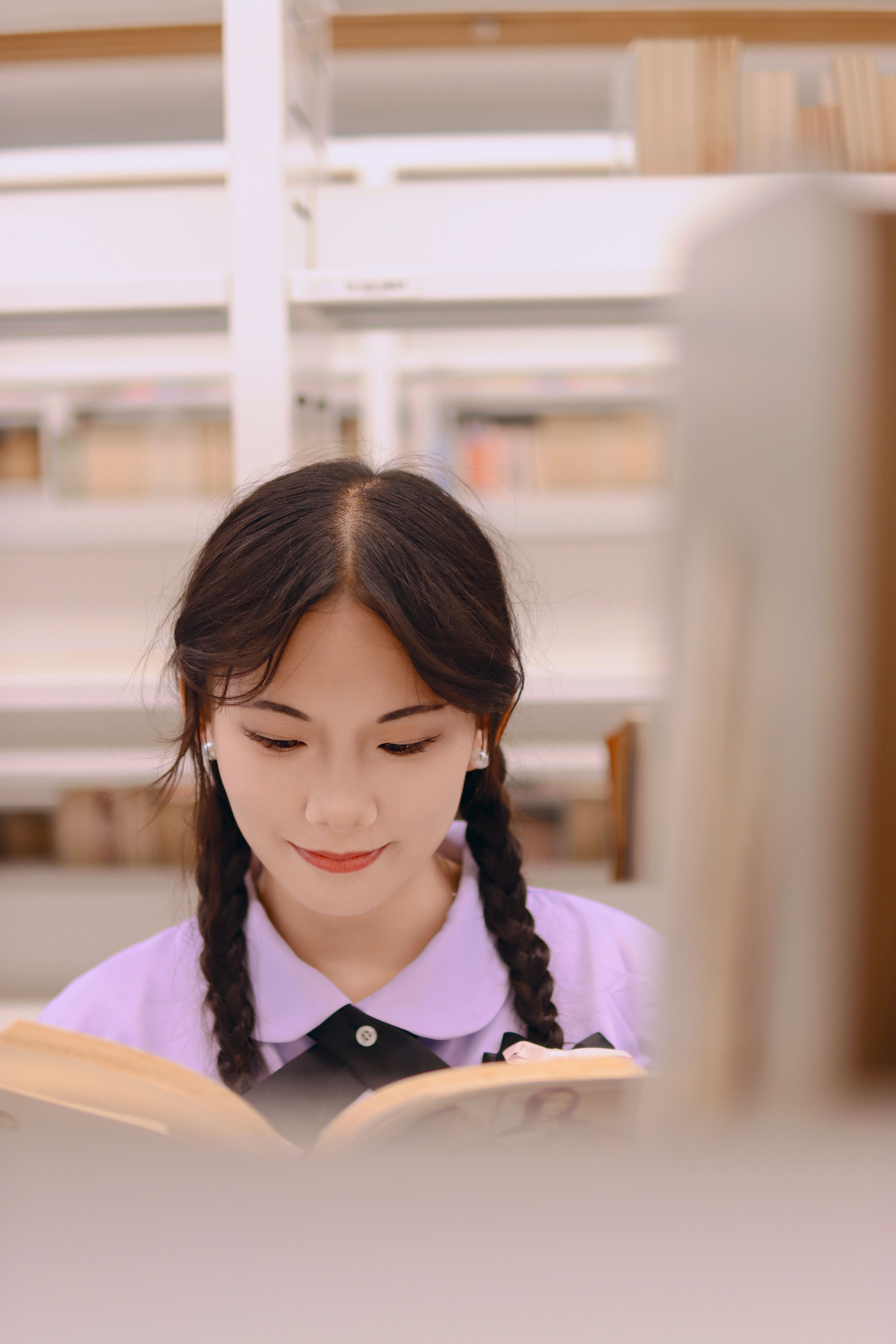 A young woman with braids engrossed in reading inside a well-lit library.