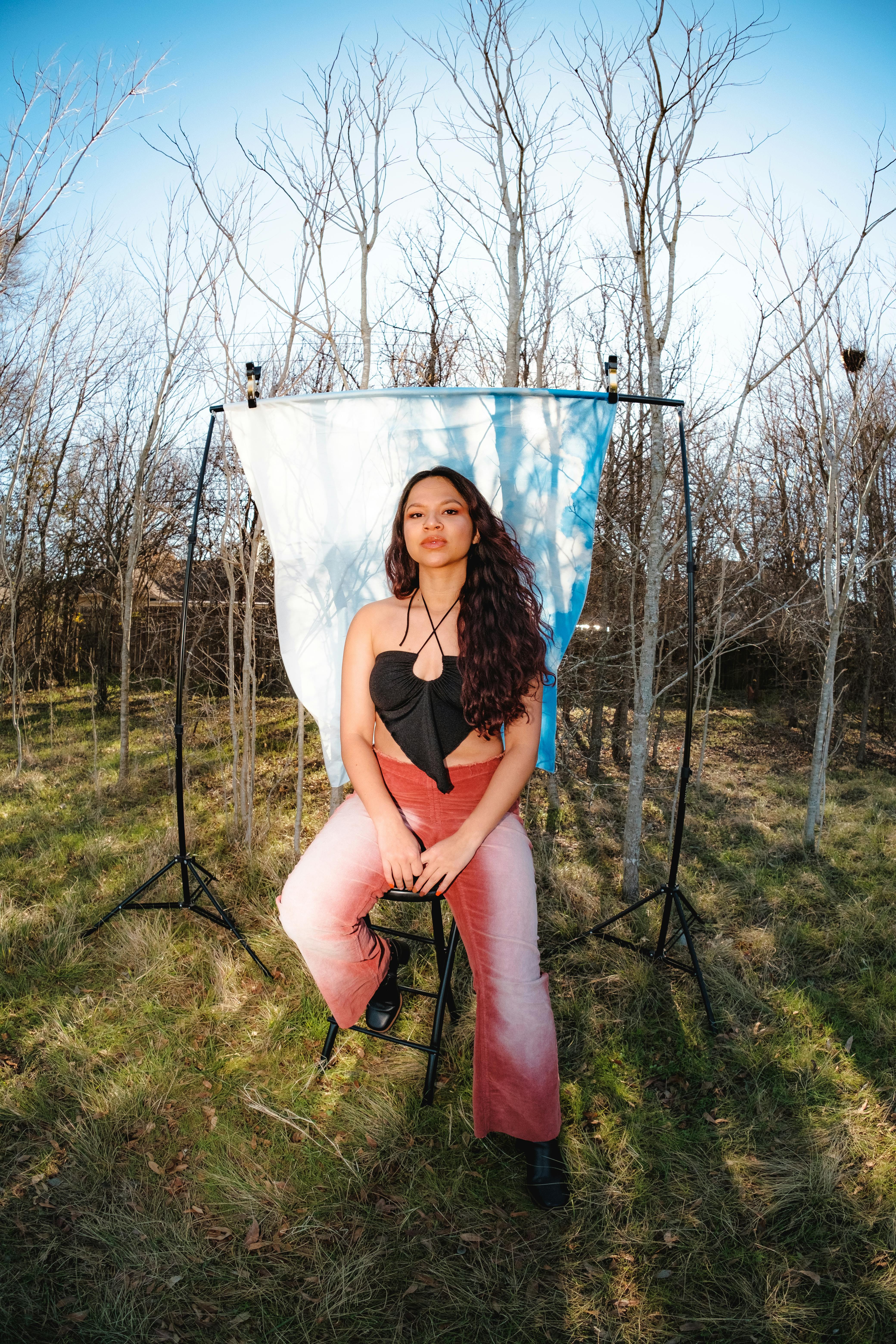Stylish young woman posing outdoors with a backdrop, blending nature and fashion.
