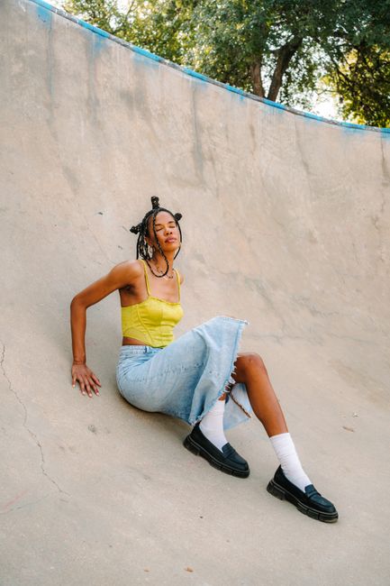 Fashionable woman in a denim skirt and yellow top posing outdoors in a skate park.