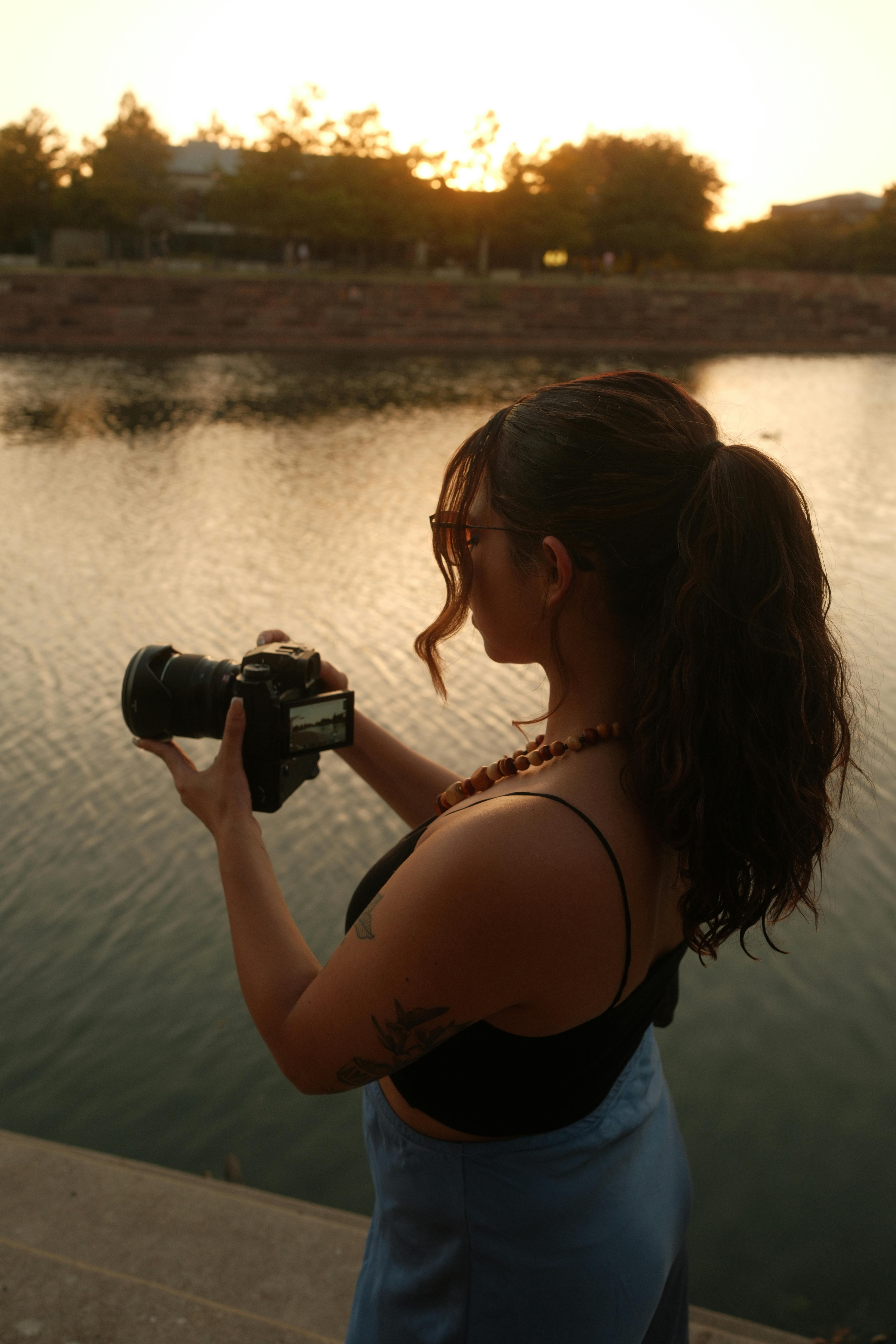 A woman capturing the serene beauty of a lake at sunset with her camera.