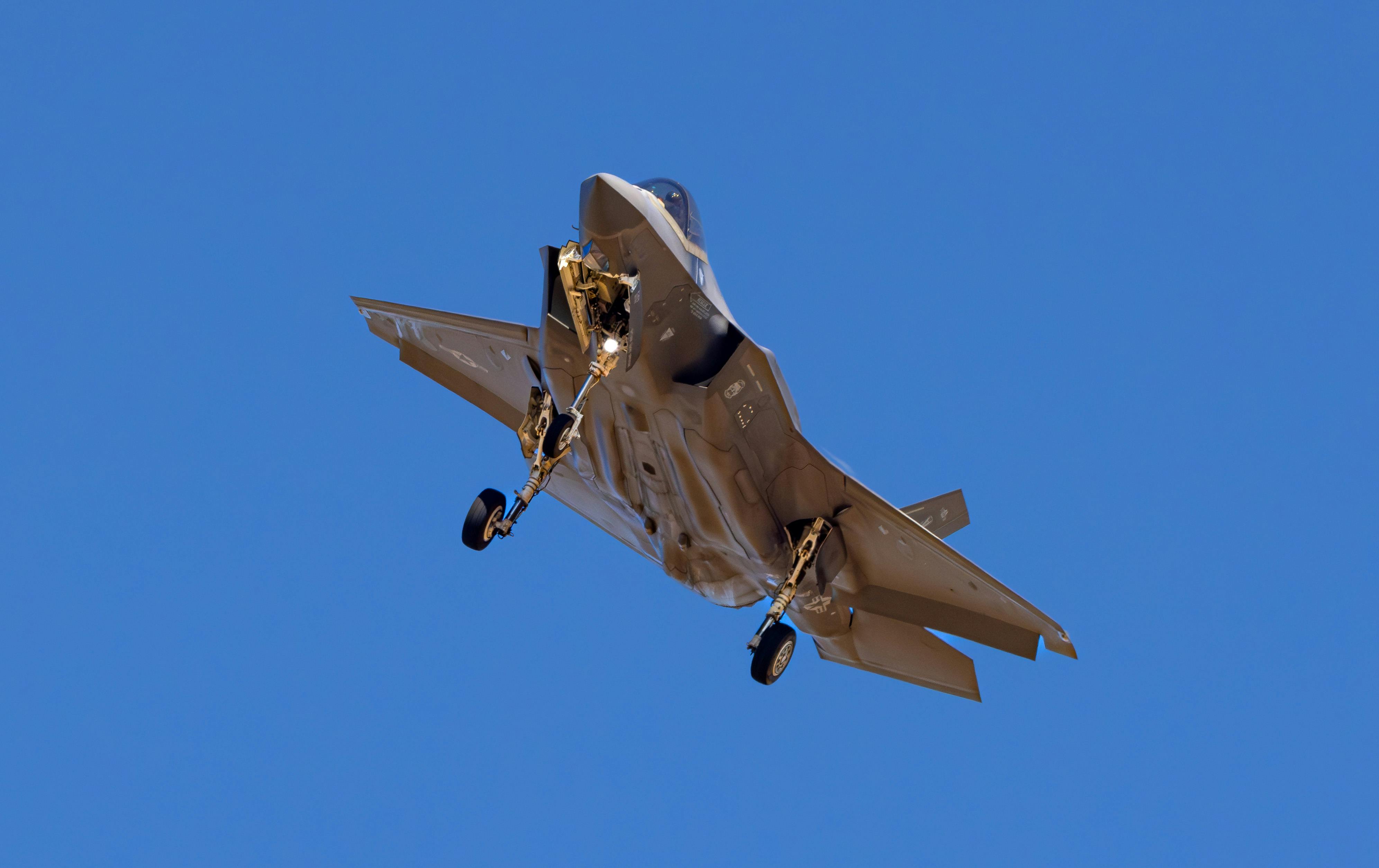 A military jet is captured flying under a bright blue sky, showcasing its aerodynamic design.