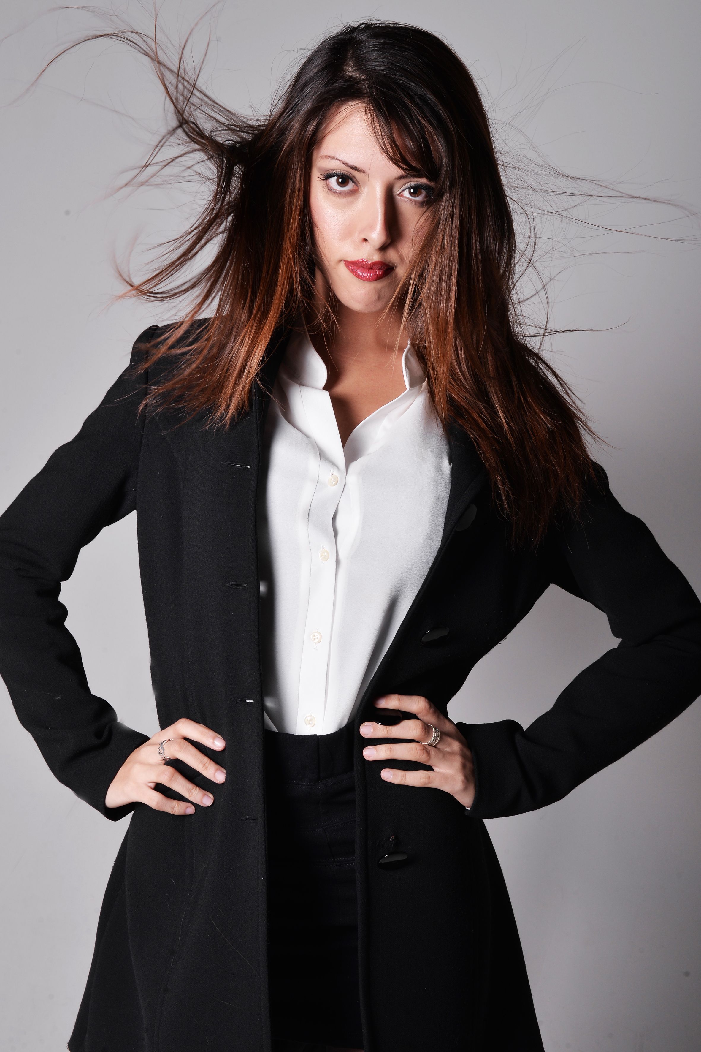 Stylish and confident woman in business attire posing with dynamic hair movement in a studio setting.