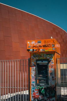 Graffiti-covered ATM booth in front of a modern building facade in Lisbon, Portugal.