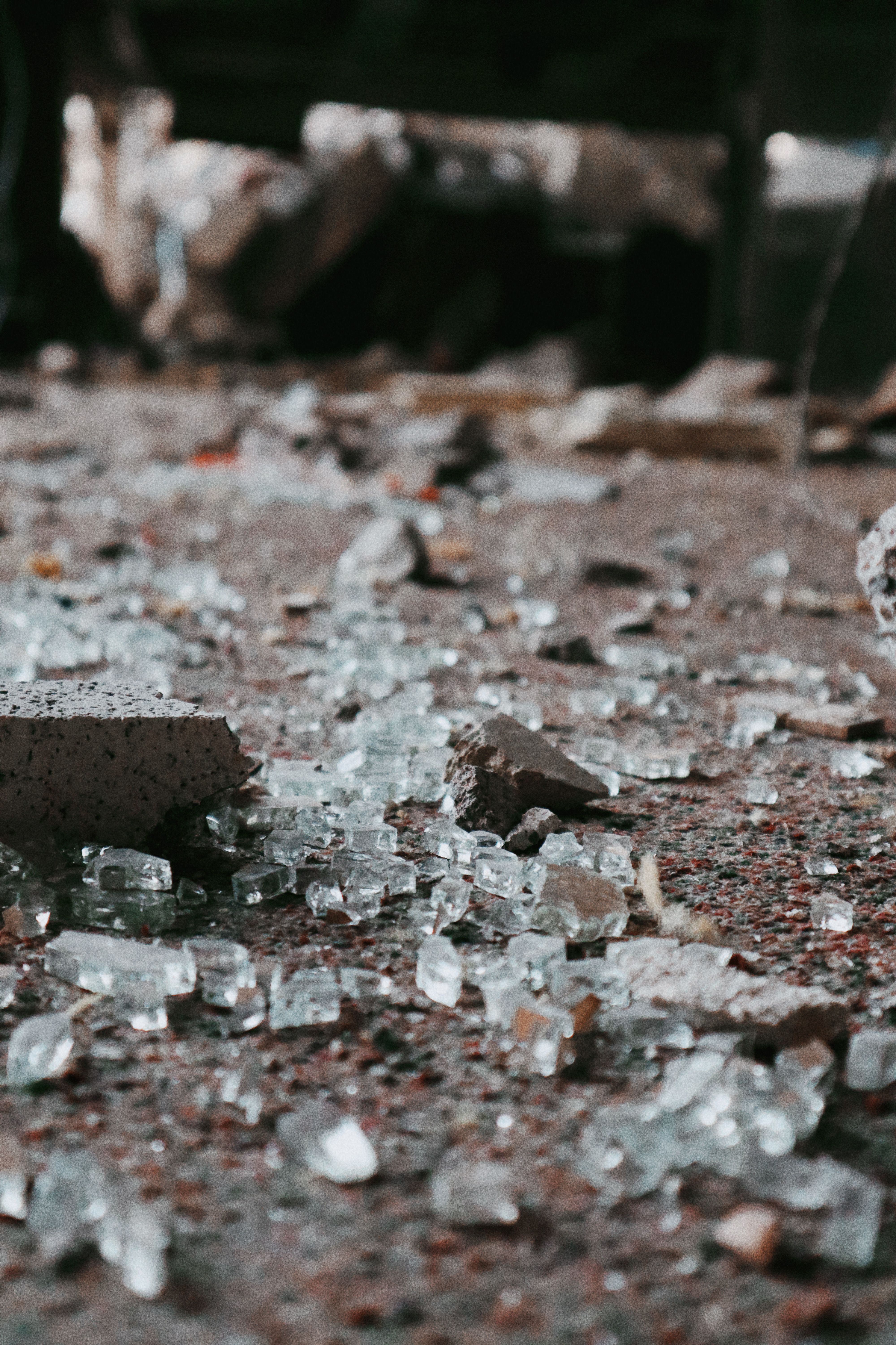 Close-up view of scattered broken glass and debris on a concrete surface in an urban setting.