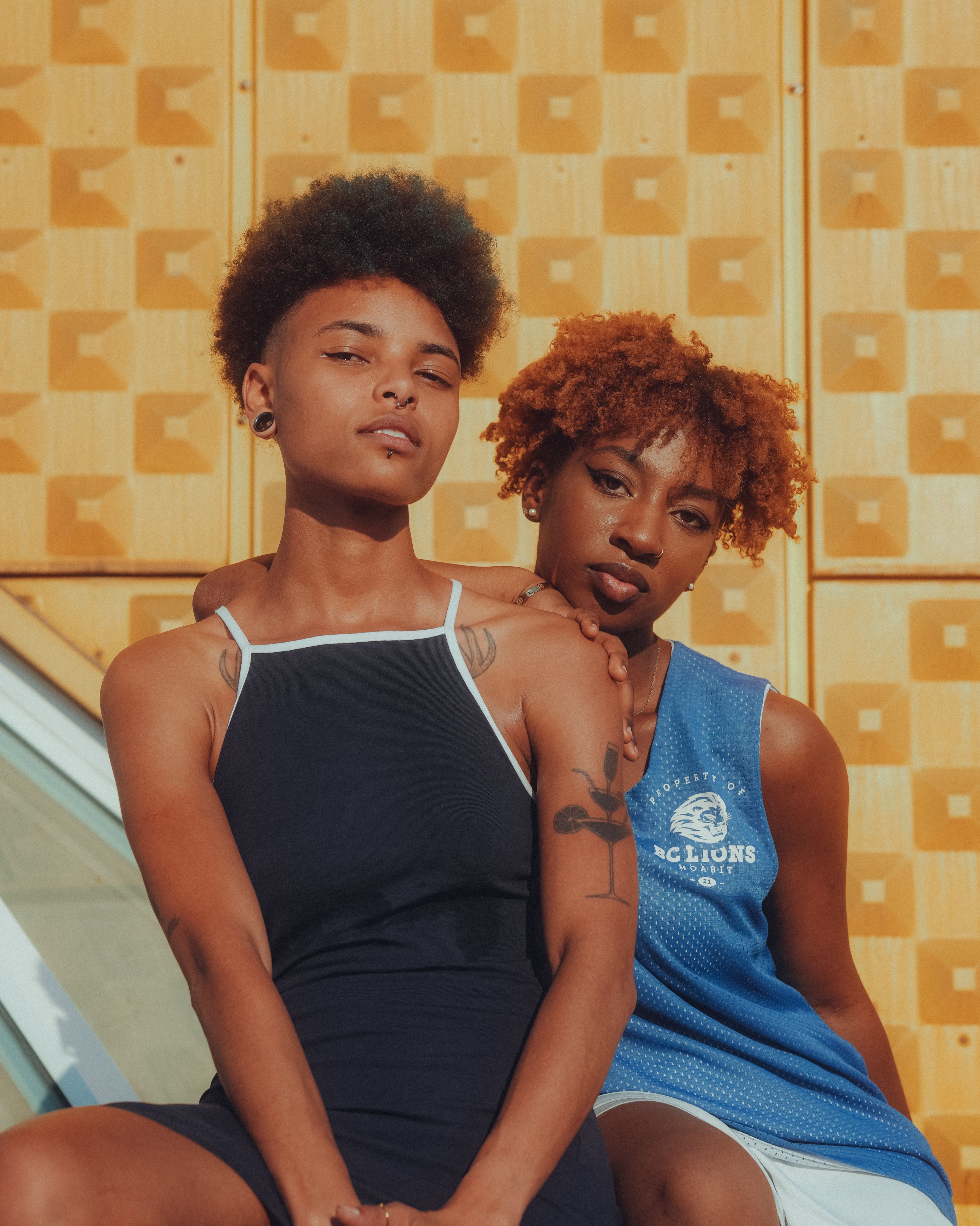 Two confident young women posing stylishly outdoors against a modern architectural backdrop.