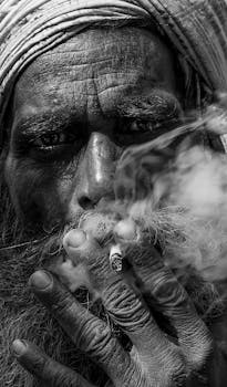 这是一幅描绘吸烟老人的黑白特写肖像，有力地展现了面部的皱纹与纹理