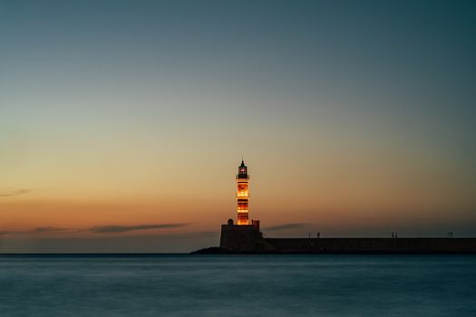Dramatic evening view of the Chania Lighthouse against a vibrant sunset in Crete, Greece.